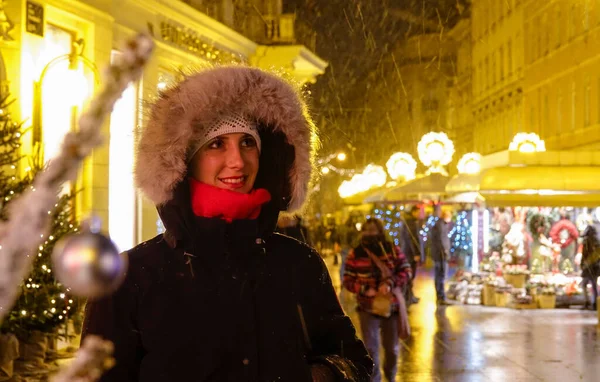 FERMETURE : Une fille souriante regarde autour du marché de l'avent par une nuit d'hiver enneigée. — Photo