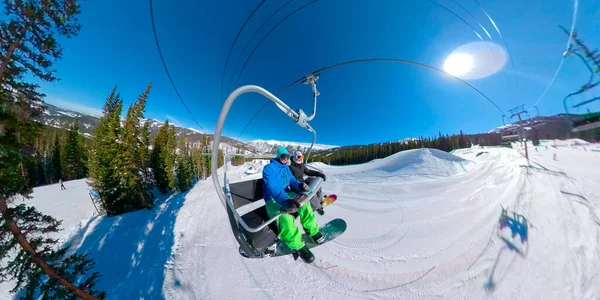 Casal de snowboarder feliz monta o teleférico em um dia ensolarado de inverno. — Fotografia de Stock