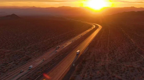 АЭРИАЛ: Пролетая над грузовиками и автомобилями, пересекающими пустыню Моджаве на закате. — стоковое фото