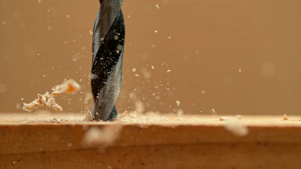 MACRO: As microplaquetas de madeira voam fora de uma prancha enquanto o handyman faz furos na peça de trabalho . — Fotografia de Stock