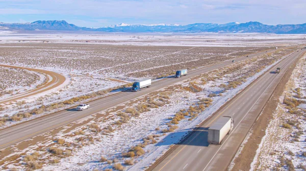 Vrachtwagens vervoeren vracht langs een snelweg door besneeuwd landschap in Utah. — Stockfoto