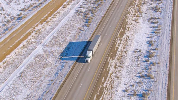 Witte vrachtwagen vervoert vracht over schilderachtige snelweg door besneeuwde woestijn. — Stockfoto