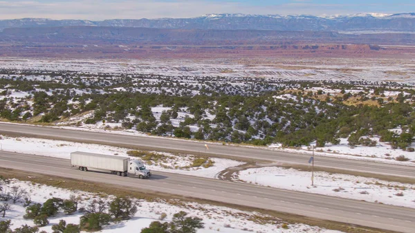 Белый грузовик везет груз по живописной автостраде, проходящей через снежную пустыню. — стоковое фото
