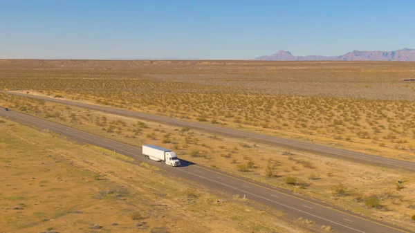 AERIAL: Witte vrachtwagen vervoert een vrachtcontainer door het dorre landschap. — Stockfoto