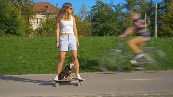 Міленіалка та її старша собака їздять на електричному скейті через парк — стокове фото