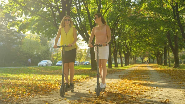 PUN FLARE: 공원 주변에 e-scooters 를 타고 있는 두 여성이 웃고 이야기하는 모습 — 스톡 사진