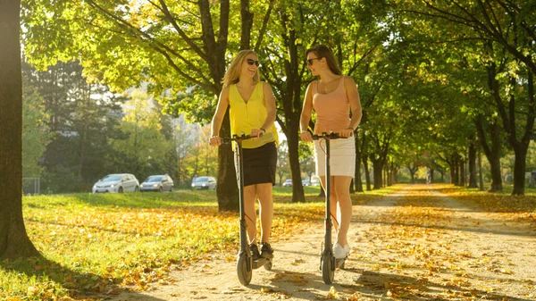 여자들은 공원을 가로지르는 경치좋은 오솔길을 따라 e-scooters 를 타는 즐거움을 즐긴다. — 스톡 사진