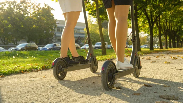 눈에 띄지 않는 두 명의 여성 친구가 화창 한 날에 e-scooter 를 타고 간다. — 스톡 사진