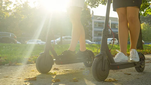 FLARE DE LA LENTE: Foto cinematográfica de mujeres en faldas montando e-scooters en un día soleado — Foto de Stock