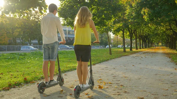 FLARE DE LA LENTE: Pareja despreocupada monta scooters eléctricos en un día soleado de otoño. — Foto de Stock