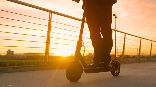 LOW ANGLE: Onherkenbare zakenman rijdt een elektrische scooter bij zonsondergang. — Stockfoto