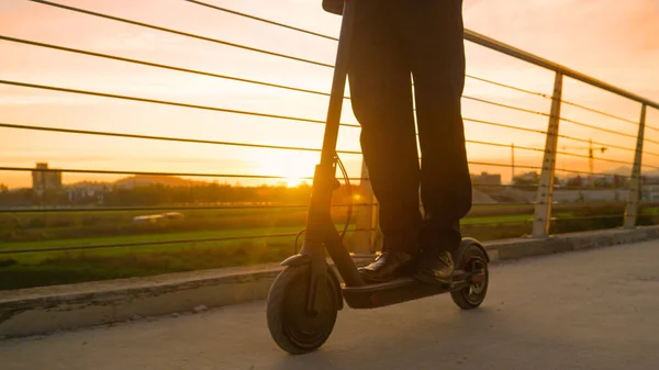 LOW ANGLE: Бізнесмен їде на електронному скутері, щоб працювати в сонячний весняний ранок . — стокове фото