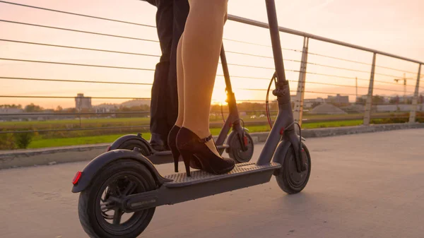CERRAR: Los cálidos rayos de sol brillan en los hombres de negocios y las mujeres que montan scooters al atardecer — Foto de Stock
