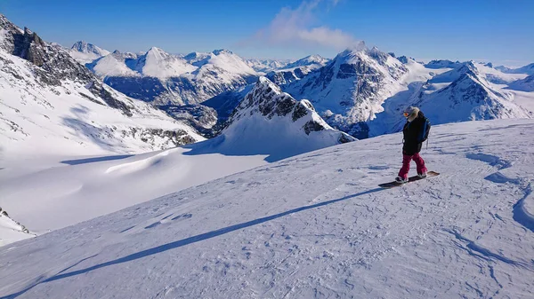 Havalı kadın snowboardcu piste çıkmadan önce dağlara bakar.