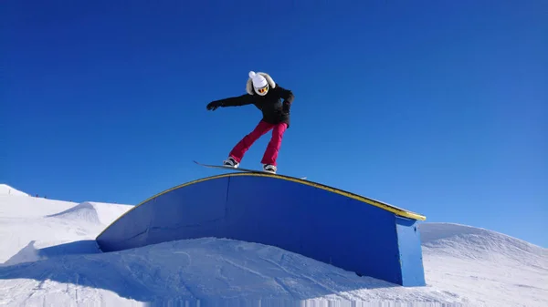 Cool snowboarder hembra hace un truco de foque a lo largo de una barandilla en un gran parque de nieve. — Foto de Stock