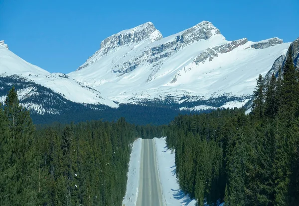 AERIAL: Spectacular view of snowy Canadian Rockies towering above empty road. — ストック写真