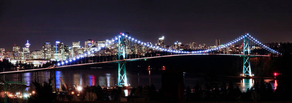 Panoramic view of illuminated skyscrapers and bridge in Vancouver on calm night.