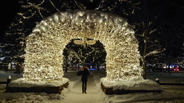 Kvinnliga turist promenader under en båge av julbelysning i en liten snöig park. — Stockfoto