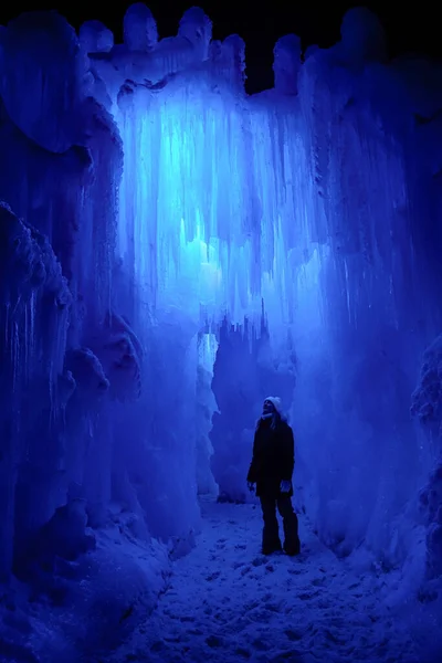 VERTICAL: Woman exploring icecave stands under a wall of massive ice stalactites — ストック写真