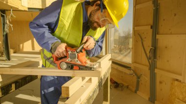 Sakallı inşaatçı inşaat alanında ahşap bir kirişi zımparalıyor.