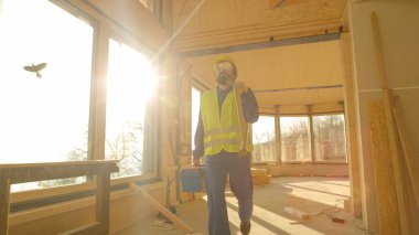 Tulum giymiş ve kasketli işçi güneşli bir sabahta işe geliyor.