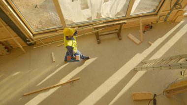 İşçi işe geliyor, alet çantasını ve merdivenini odanın diğer tarafına taşıyor..