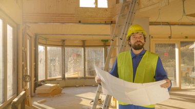 Proje yöneticisi planlara ve inşaat halindeki bir eve bakıyor..