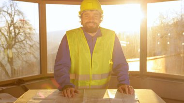 Güneş doğarken kat planlarını inceledikten sonra statik teknisyen gülümsüyor..