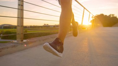 Atletik genç adam güneşli bir akşamda asfalt bir köprüde koşuyor..