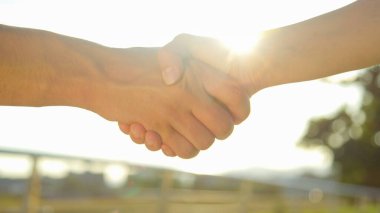 CLOSE UP: Two business partners shake hands in the park on a sunny spring day.