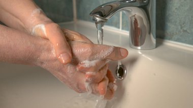 Tanınmayan yaşlı kadın ellerini sabun ve suyla yıkıyor..