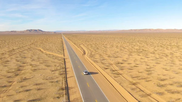 Vliegen achter een zilverkleurige auto terwijl hij over een snelweg door de woestijn rijdt. — Stockfoto