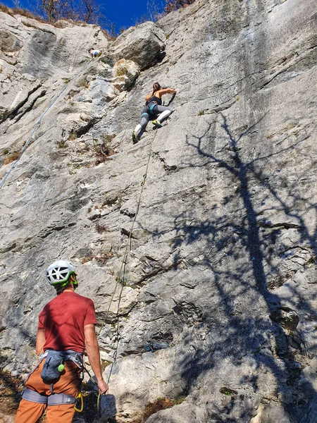VERTICAL Mann hält die Sicherungsseile und schaut auf, wie Freund Felswand erklimmt. — Stockfoto