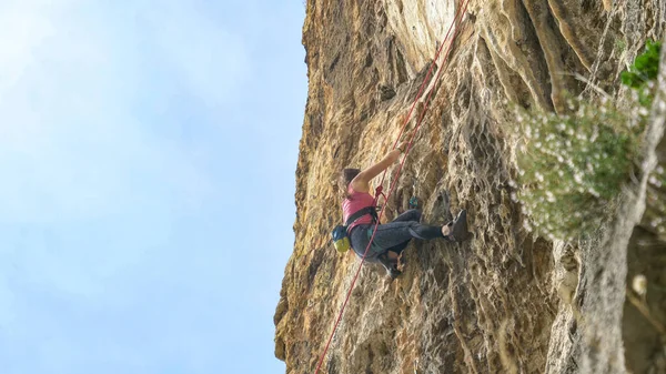 Young woman fearlessly climbs up a rocky cliff on perfect day for rock climbing — Stock Photo, Image