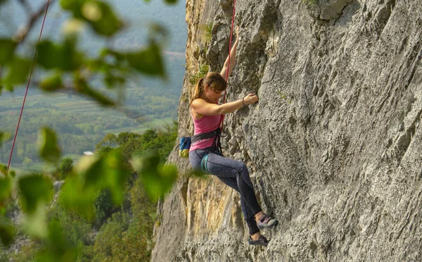 CHIUDI: Giovane arrampicatrice femminile scala una scogliera massiccia in una giornata di sole. — Foto Stock