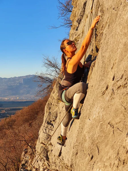 VERTICAL: Athletic woman wearing sunglasses climbs up a challenging rocky wall. — Stock Photo, Image