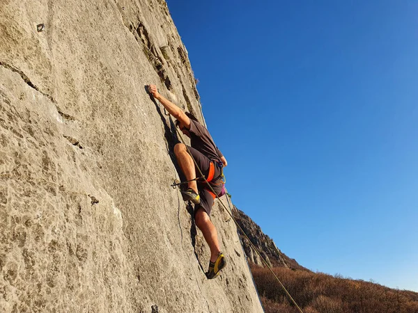 Young man fearlessly climbs up a rocky cliff on perfect day for rock climbing — ストック写真