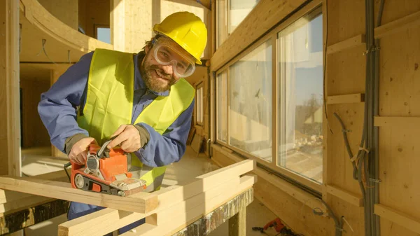 Ritratto: Costruttore sorridente che lavora su una casa prefabbricata lucida una trave di legno. — Foto Stock
