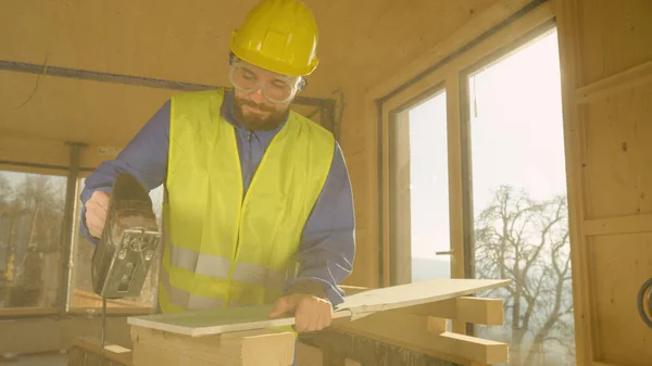 LENS FLARE: Il lavoratore che costruisce una casa in legno di latifoglie sta tagliando un wallboard di gesso. — Foto Stock