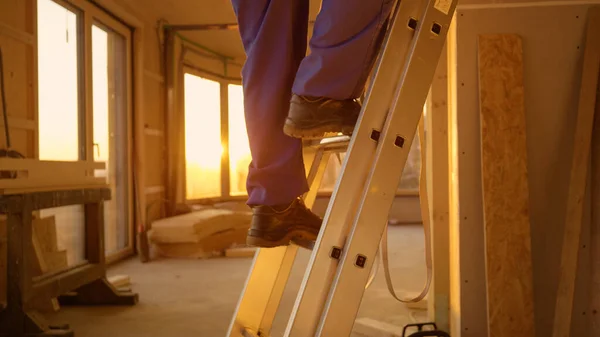 LENS FLARE: Costruttore in tuta blu scende una scala in alluminio al tramonto. — Foto Stock