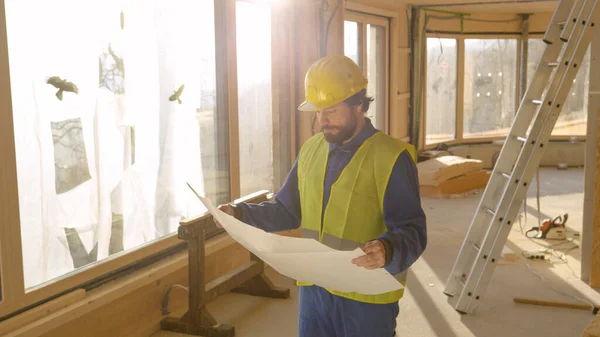 Κοντινό πλάνο: Ο διαχειριστής του έργου εξετάζει τα σχέδια και ένα σπίτι υπό κατασκευή. — Φωτογραφία Αρχείου