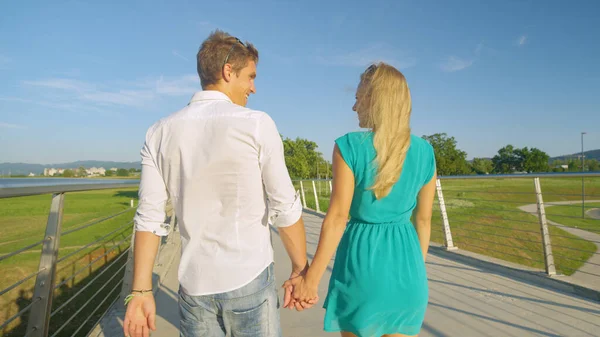 FERMETURE : Heureux jeunes chéris tenant la main traversent un pont par une journée ensoleillée. — Photo