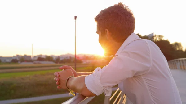 CERRAR: Un joven empresario irreconocible mira la impresionante puesta de sol dorada. —  Fotos de Stock