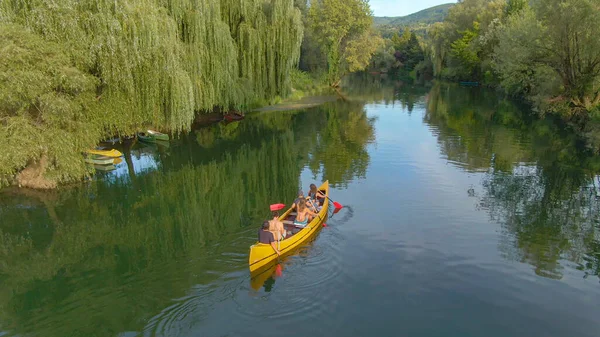 AERIAL: Voando acima de um grupo de amigos remando uma grande canoa ao longo do rio calmo. — Fotografia de Stock