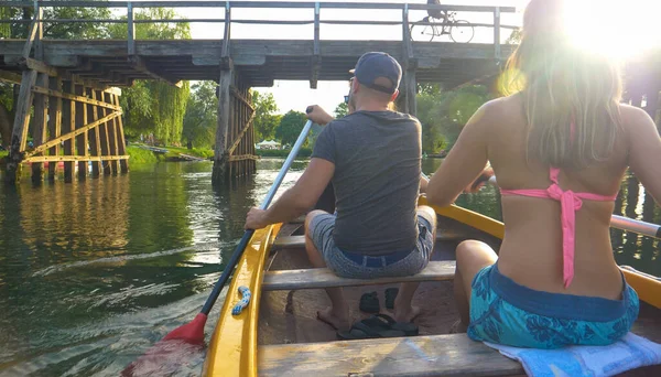 CLOSE UP: Homem e mulher remam uma canoa ao longo de um rio calmo e sob uma ponte — Fotografia de Stock