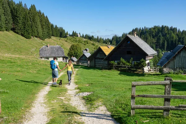 Man and woman walk toward a village of wooden houses in Slovenian mountains. — 图库照片