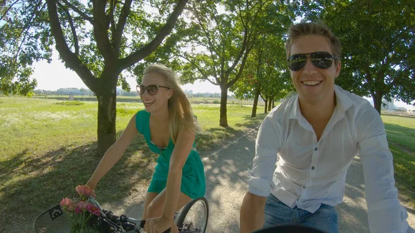 SELFIE: Los rayos del sol brillan en la pareja de turistas felices montando bicicletas alrededor de un parque — Foto de Stock