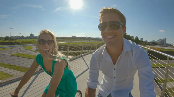 SELFIE: Handsome man and his girlfriend ride their bicycles across modern bridge — ストック写真