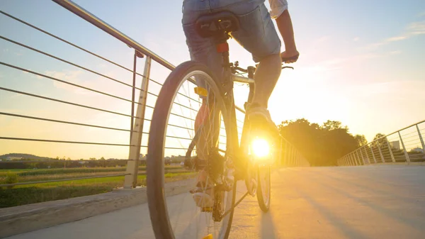 LENS FLARE: Nierozpoznawalny mężczyzna pedałuje rowerem po wiadukcie o wschodzie słońca. — Zdjęcie stockowe