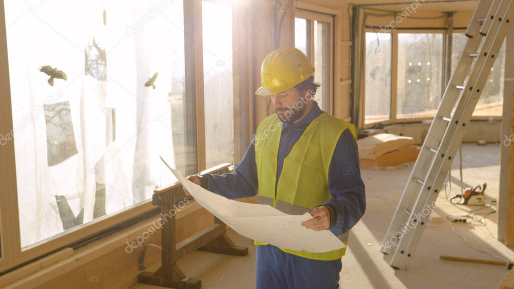 CLOSE UP: Project manager looks at the plans and a house under construction.